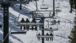 Skiers and snowboarders ride a high speed chairlift.