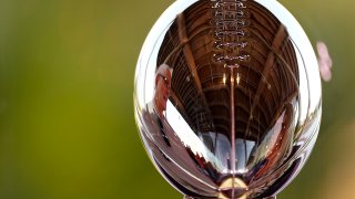 A man is reflected in the Lombardi Trophy