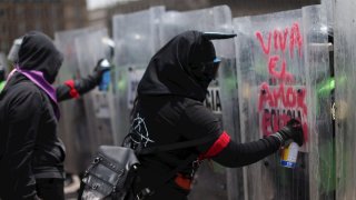 Mujeres vestidas de negro pintan un mensaje de amor en escudos policiales