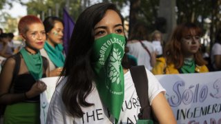 Mujer joven con un pañuelo verde cubriendo parte de la cara en una manifestación a favor del aborto