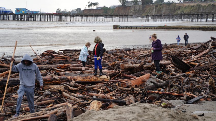 People walk among driftwood storm debris on the beach in Capitola.
