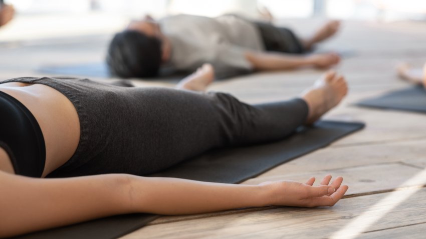 Unrecognizable woman lying on mat in corpse pose while practicing yoga in studio, meditating while making shavasana exercise, attenting meditation training class, cropped image with free space