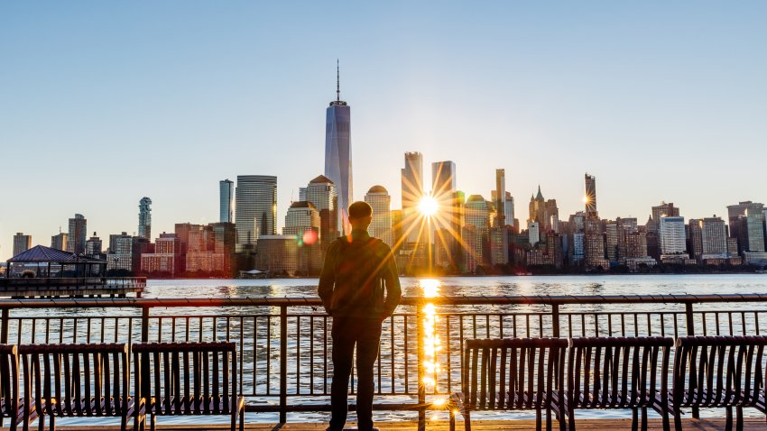 Rear view of a man looking at New York City skyline at sunrise.