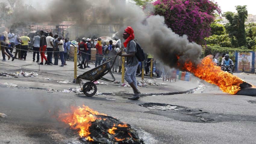 Un hombre empuja una carretilla frente a neumáticos en llamas durante una protesta para exigir la renuncia del primer ministro Ariel Henry, el jueves 7 de marzo de 2024, en Puerto Príncipe, Haití. (AP Foto/Odelyn Joseph)