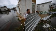 A man carries a piece of corrugated iron in a flooded street after the passage of Hurricane Rafel in Batabano, Mayabeque province, Cuba, on November 7, 2024. Hurricane Rafael knocked out power to all of Cuba on Wednesday as it slammed through the cash-strapped island, which was still reeling from a recent blackout and a previous deadly storm. Rafael strengthened to a major Category 3 hurricane as it made landfall on the Caribbean island of 10 million people. (Photo by Yamil LAGE / AFP) (Photo by YAMIL LAGE/AFP via Getty Images)