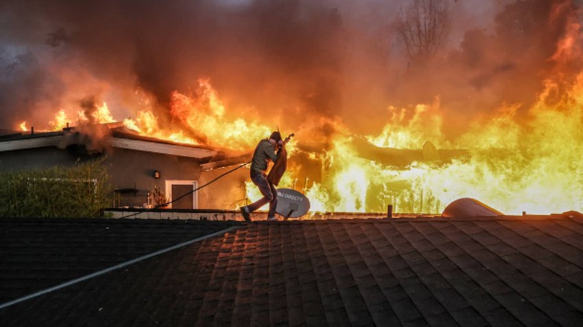 Steve Salinas shields himself from intense heat as he hoses down a neighbor’s rooftop in Altadena, California, as wildfires rage in the Los Angeles area, Jan. 8, 2025.