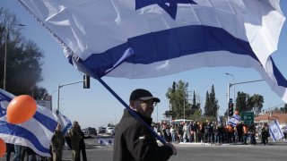 Israelíes esperan en la carretera el paso de la comitiva fúnebre de Shiri Bibas y sus dos hijos, Ariel and Kfir, que murieron durante su cautiverio en Gaza, cerca del kibbutz Yad Mordechai, en Israel, el 26 de febrero de 2025.