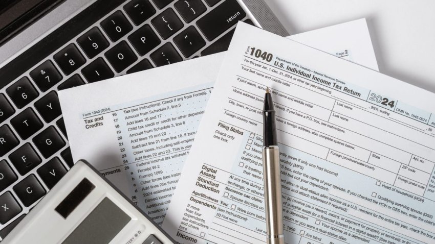 A close-up of a 1040 U.S. Individual Income Tax Return form, placed on a laptop keyboard with a pen and calculator.