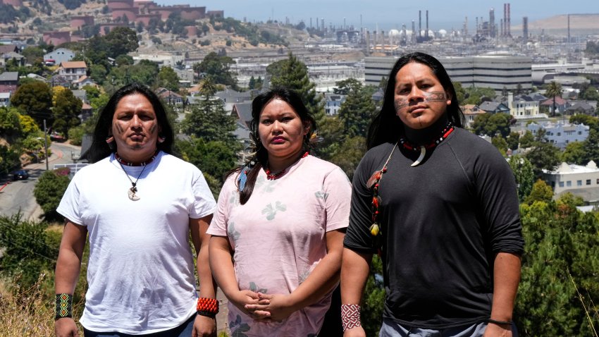 De izquierda a derecha, Juan Bay, presidente del pueblo waorani de Ecuador; Jhajayra Machoa Mendúa y Nadino Calapucha, portavoz del pueblo kichwa pakkiru, posan para una fotografía mientras al fondo puede verse una refinería de Chevron, el jueves 19 de junio de 2025, en Richmond, California. (AP Foto/Godofredo A. Vásquez)