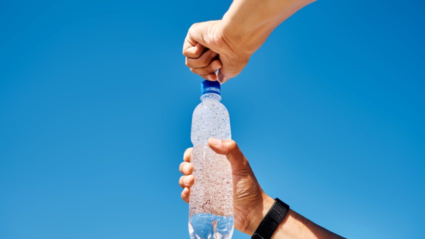 Men’s hands open a plastic bottle of sparkling water against the blue sky.