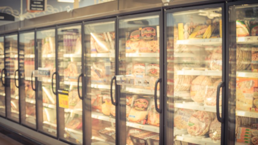 Blurred variety pack of processed pizza at retail store in America. Frozen food section in huge glass door aisle. Freezer full assortment of frozen pizza in local supermarket, defocused background